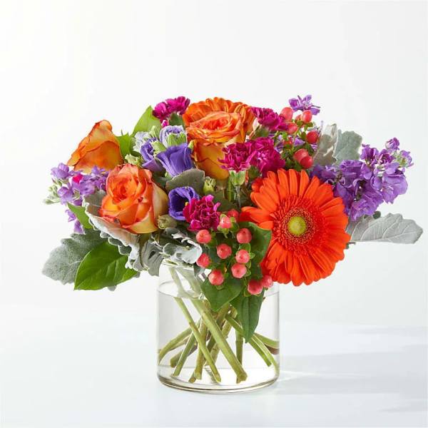 Mixed bouquet of orange, purple, and pink flowers in a clear glass vase