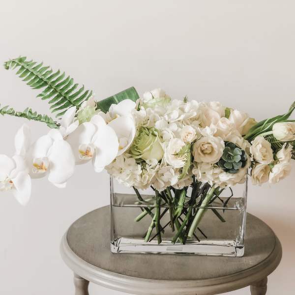 White orchid and cream floral arrangement in a clear rectangular vase
