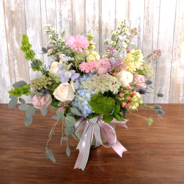 Pastel bouquet of roses, gerbera daisies, and hydrangeas in a glass vase with striped and pink ribbons