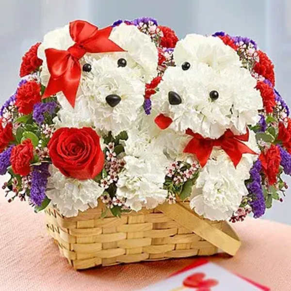 Two white floral dog figures in a wicker basket with red bows and roses