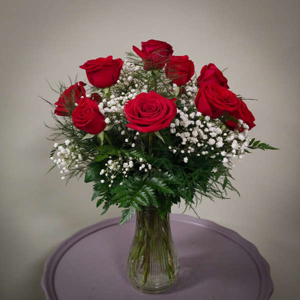 Red roses arranged in a clear glass vase with white baby's breath