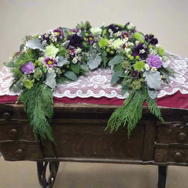 Floral casket spray with purple, white, and green flowers