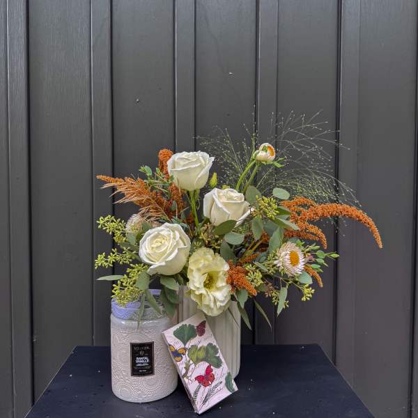 White roses and pale blooms in a vase with a candle and gift box