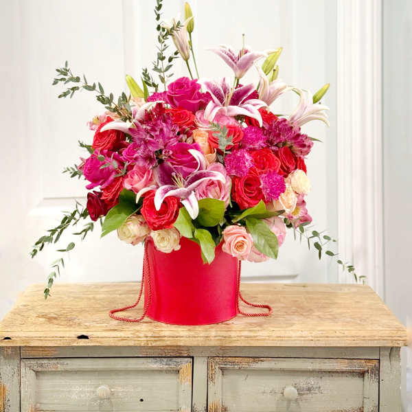 Pink and red floral arrangement in a red hatbox