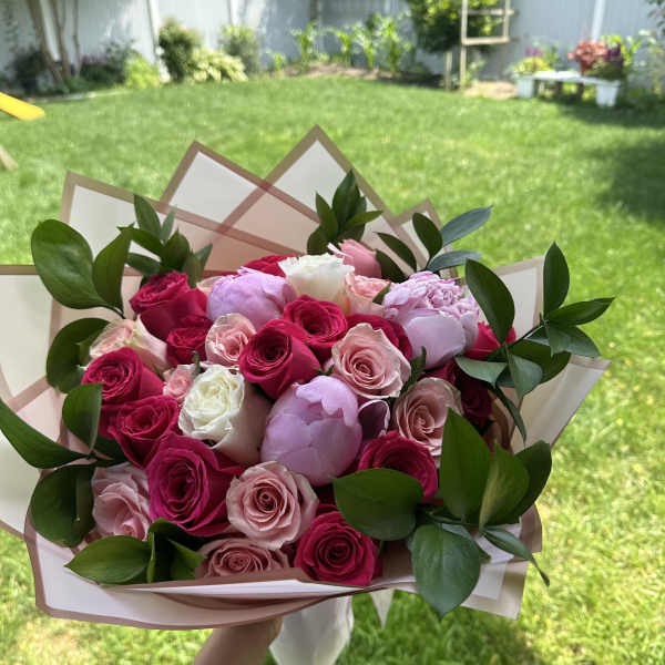 Handheld bouquet of pink, white, and red roses with greenery