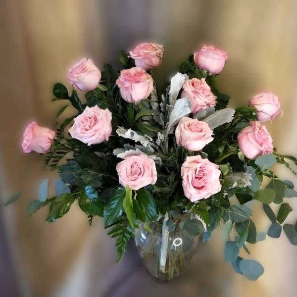 Pink roses arranged in a clear glass vase with mixed greenery.