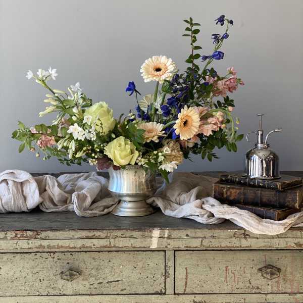 Mixed flower arrangement in a silver vase with peach, white, and blue blooms