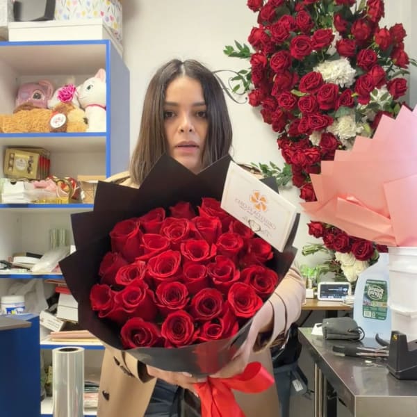 Woman holding a bouquet of red roses wrapped in black paper with a red ribbon