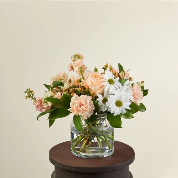 Low bouquet of peach roses, carnations, and white daisies in a clear glass vase