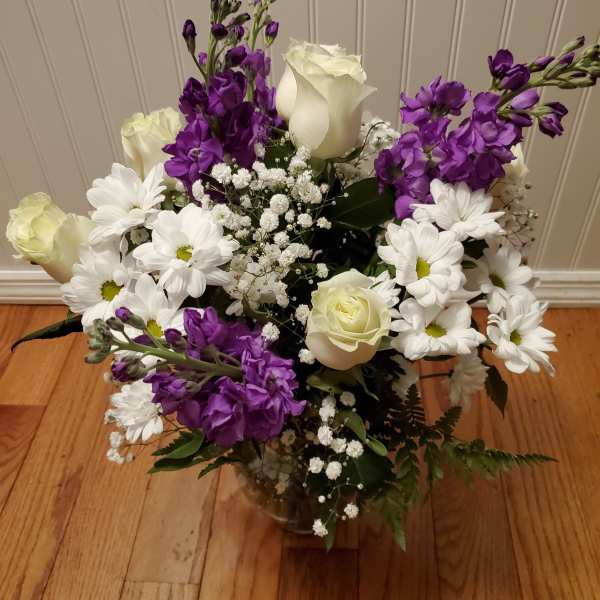 Mixed bouquet of white roses, white daisies, and purple flowers arranged in a clear glass vase