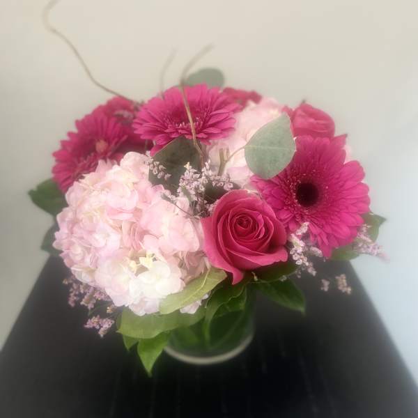 Pink gerbera daisies, a rose, and pale hydrangea in a glass vase