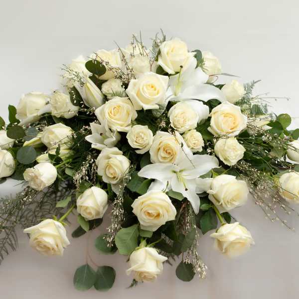 White rose and lily arrangement with greenery on a white surface