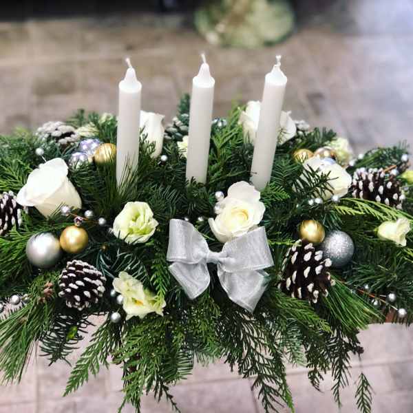 Holiday centerpiece with white candles, roses, pinecones, and a silver bow