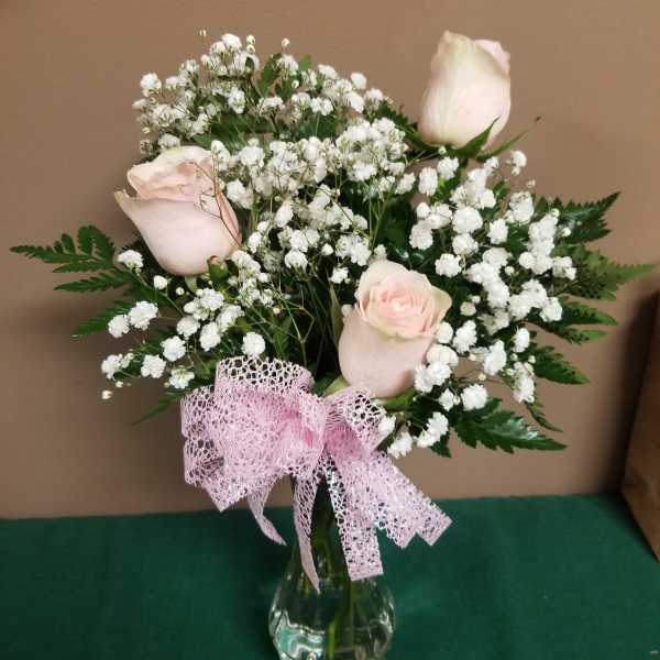 Pale pink roses and baby's breath in a clear glass vase with a pink ribbon