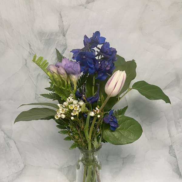 Mixed bouquet of blue, lavender, and white flowers in a clear glass vase