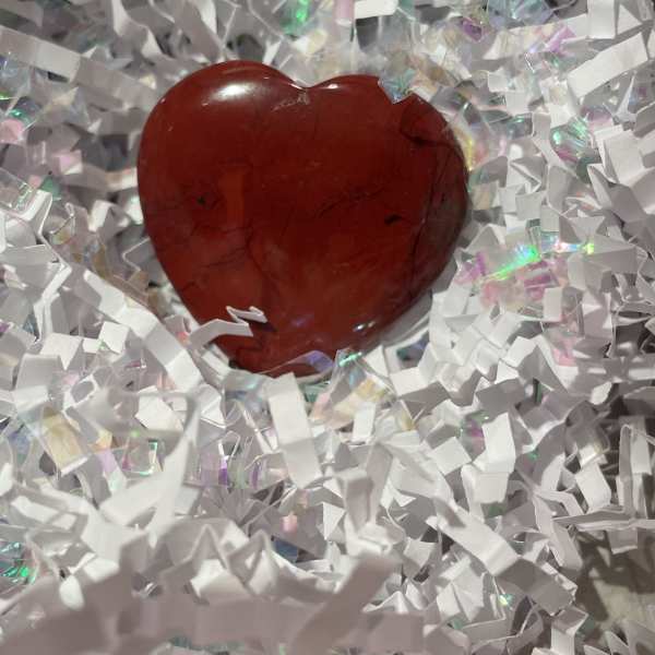 Red polished heart-shaped stone nestled in white crinkle paper filling