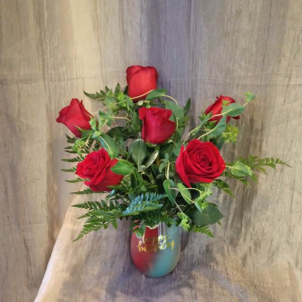 Red roses arranged in a multicolor vase with greenery