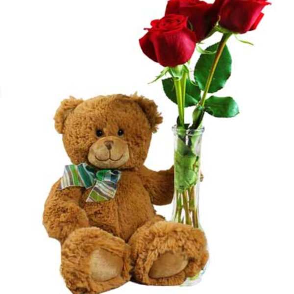 Teddy bear beside a glass vase with three red roses