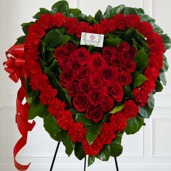 Heart-shaped standing wreath of red roses and carnations with greenery and a red ribbon