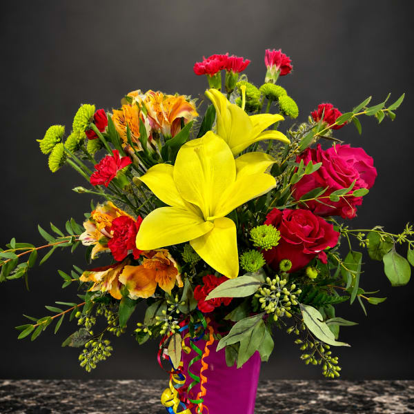Bright mixed bouquet with yellow lilies, red roses, and a magenta vase