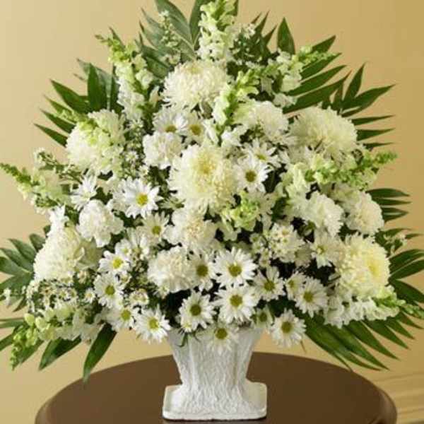 Tall white sympathy arrangement of daisies, mums, and snapdragons in a white urn-style vase