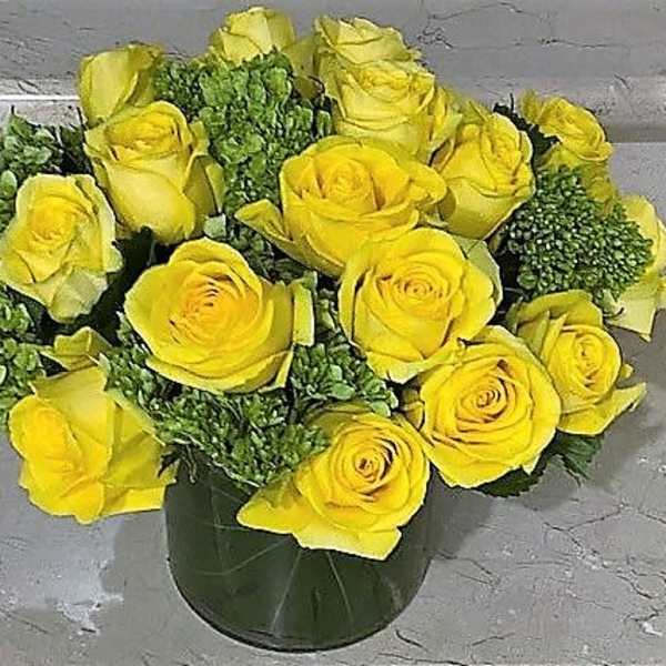Low arrangement of yellow roses with green accents in a clear glass cylinder vase