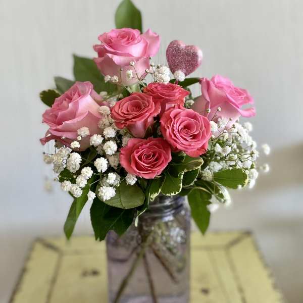 Pink roses in a glass jar with baby's breath and a glittery heart pick