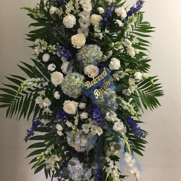 Large standing floral spray with white and blue flowers and a ribbon tribute