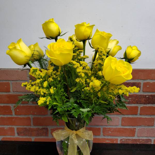 Arrangement of yellow roses with yellow filler flowers in a clear glass vase tied with a sheer gold bow.
