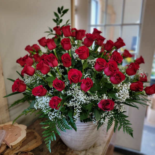Red roses arranged in a white vase with baby's breath