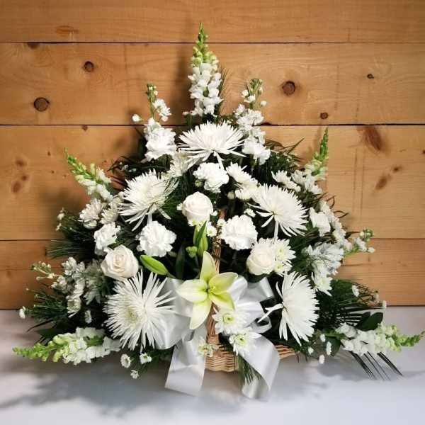White floral arrangement in a wicker basket with a white ribbon