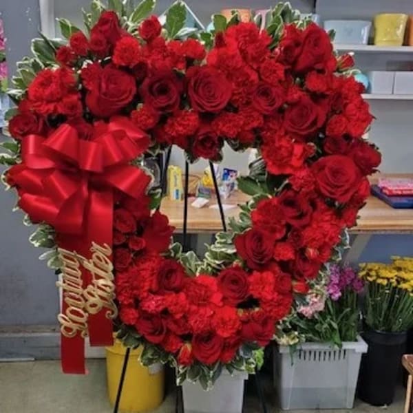 Heart-shaped red rose wreath on an easel with a large red bow