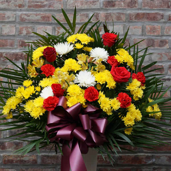Standing floral spray with red, yellow, and white flowers and a purple ribbon