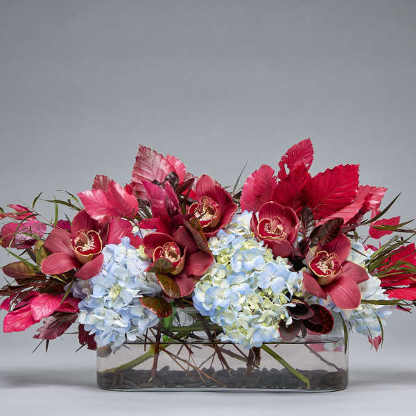 Low floral arrangement with blue hydrangeas and burgundy orchids in a glass vase