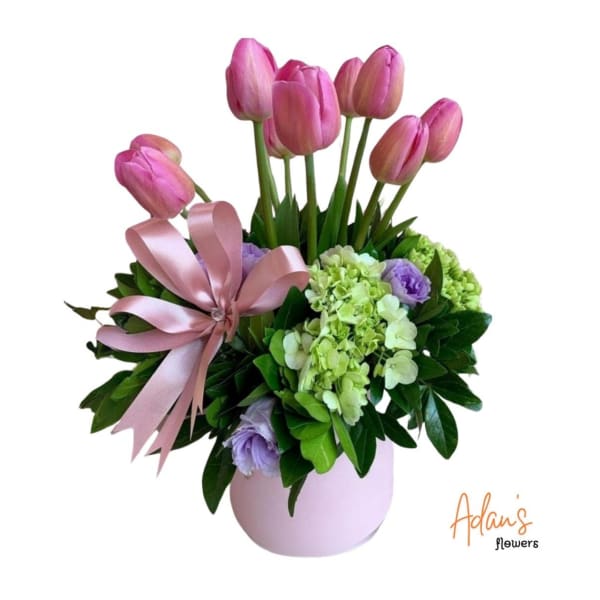 Pink tulips and pastel flowers in a lavender vase with a satin bow