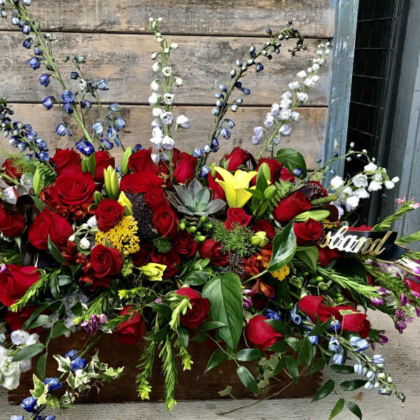Large red rose arrangement with blue and white accent flowers in a wooden box