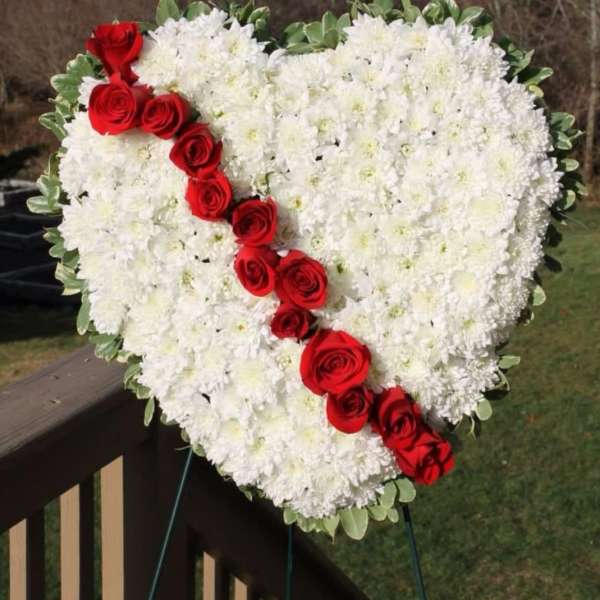 Heart-shaped standing wreath of white flowers with a diagonal line of red roses.