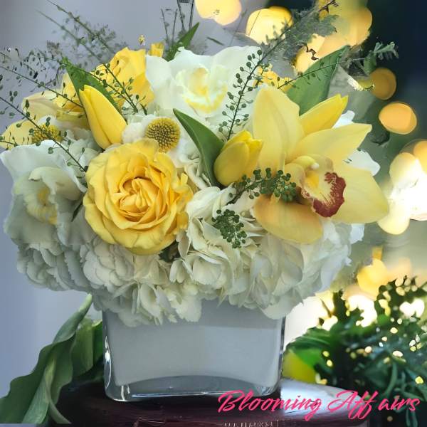 Yellow and white floral arrangement in a square glass vase