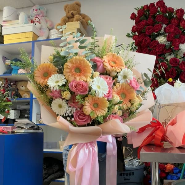 Large bouquet of pink roses and peach gerbera daisies wrapped in blush paper