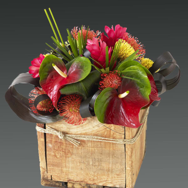 Tropical floral arrangement in a wooden box with red anthuriums and pink blooms