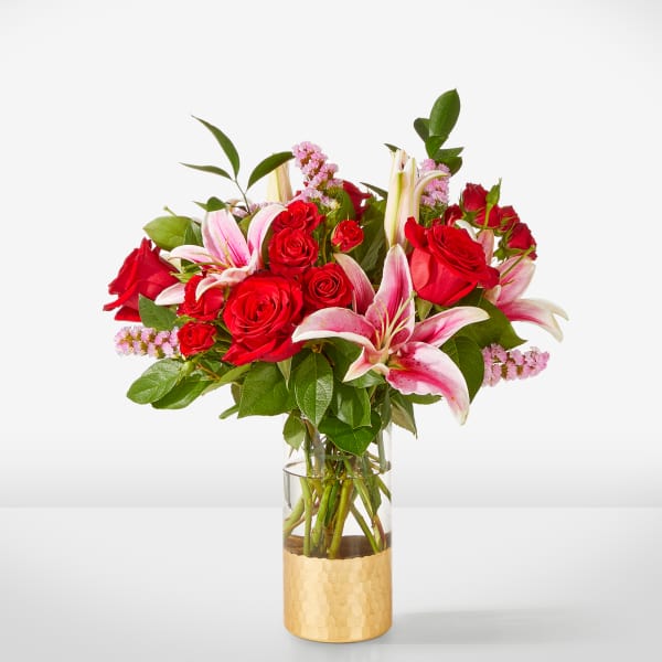 Red roses and pink lilies in a clear vase with a gold base