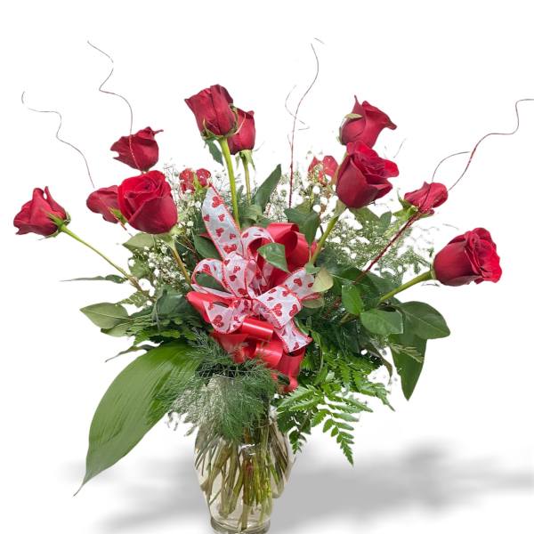 Red roses arranged in a clear glass vase with a heart ribbon