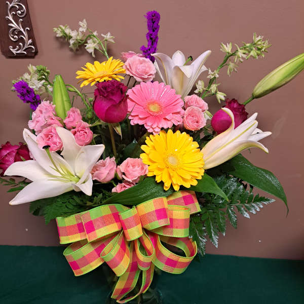 Mixed bouquet with lilies, gerbera daisies, roses, and a plaid ribbon in a glass vase
