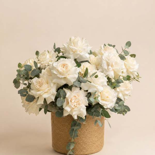 White roses arranged in a woven basket with eucalyptus