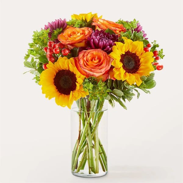 Bouquet of sunflowers, roses, and purple blooms in a clear glass vase