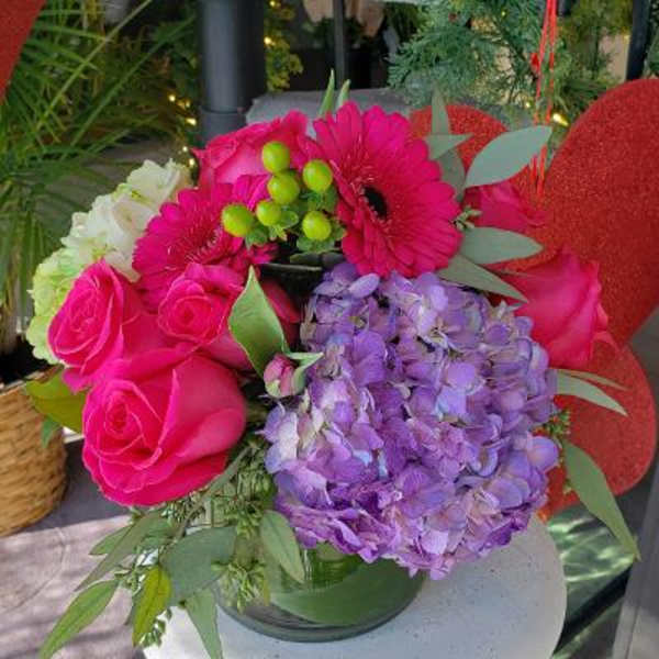 Bouquet of pink roses, purple hydrangea, and magenta gerbera daisies in a glass vase