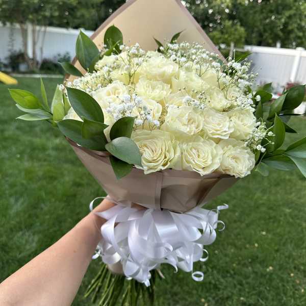 Bouquet of cream roses with baby's breath and greenery, wrapped in tan paper with a white ribbon