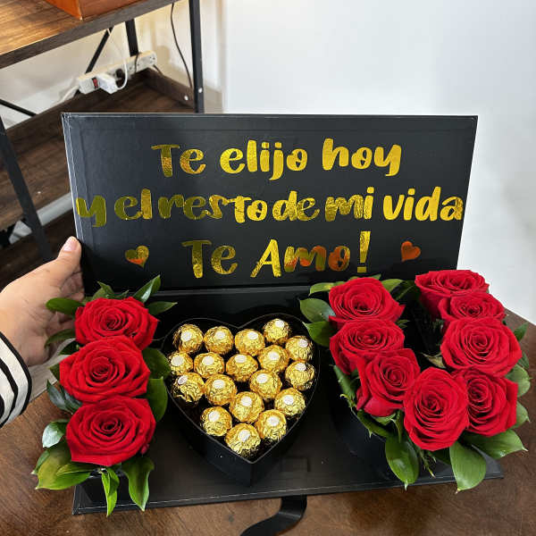 Red roses and gold-wrapped chocolates in a black gift box with a love message