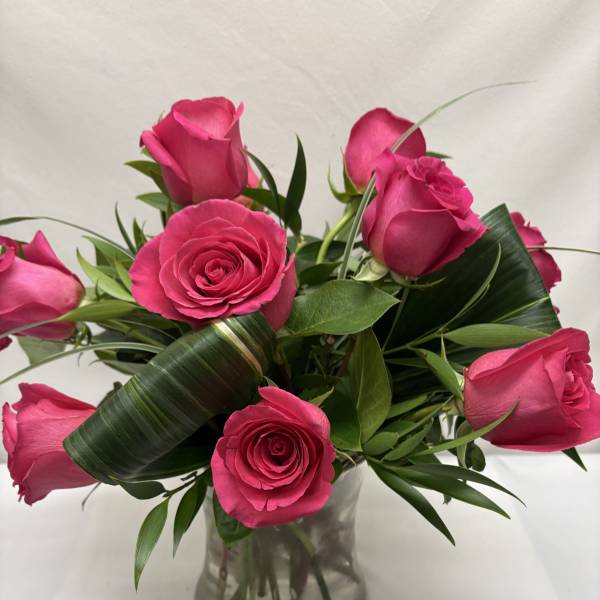 Short arrangement of hot pink roses with looped green leaves in a clear glass vase.