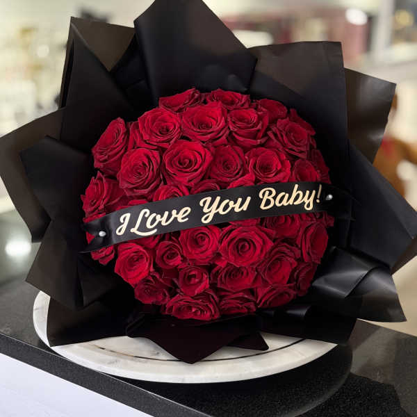 Bouquet of red roses wrapped in black paper with a "I Love You Baby!" ribbon